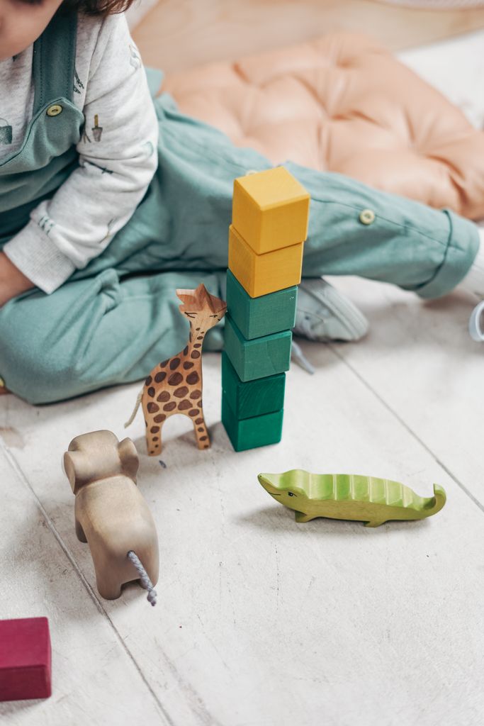 A child plays with colorful wooden toys and blocks on a wooden floor.